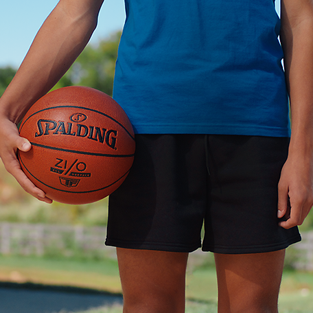 Male model in a royal blue top and a black shorts holding a Spalding Zi/O Basketball.